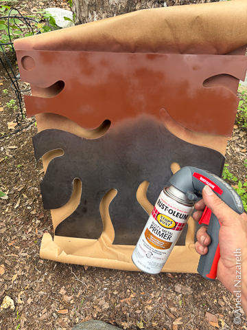 The tentacle sheet is resting on a piece of brown paper leaning against a tree. A spray can of primer held with a pistol grip handle. The top third of the sheet is primed